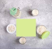 Glasses, glass mason mug with rice milk, bowl and jar with rice seeds and green copy space on concrete background. photo