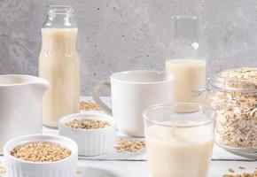 Close-up set of glass containers with oat milk, oat seeds and flakes on white table on concrete background. photo