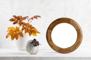 Minimal fall holidays image. Round frame, ceramic pumpkin, color leaves on table on white. Mock up. photo