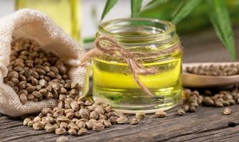 Close-up glass jar with hemp oil and cannabis seeds in sack and in wooden spoon on old wooden board. photo