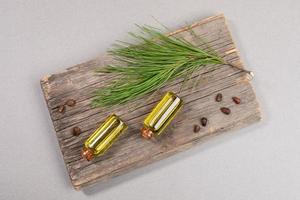 Top view two small glass bottles of essential cedar oil on old wooden board with cedar branch and nuts on grey. photo