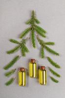 Green spruce twigs and small glass bottles of essential fir oil laid out as Christmas tree on grey textured backdrop. photo