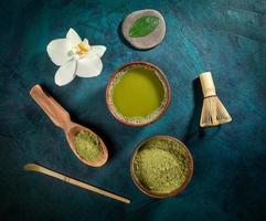 Set for cooking matcha tea cups with tea and powder, whisk, spoons, leaf, Orchid flower laid out on emerald backdrop. photo