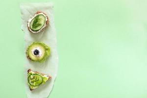 Three vegetarian sandwiches on parchment paper piece on green background. photo