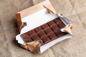 Chocolate bar in paper wrapper is lying on burlap. photo