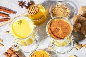 Organic turmeric milk. Two glasses for mulled wine with golden milk with ingredients on light grey backdrop with shadows. photo