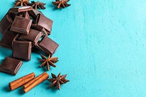 Heap of slices of chocolate, cinnamon sticks and stars anise on turquoise background. photo