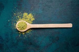 Top view of wooden spoon filled with green matcha tea powder with a little bit powder spilled out on emerald backdrop. photo