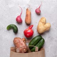 Ripe ugly vegetables scattered out of paper bag on grey concrete background. photo