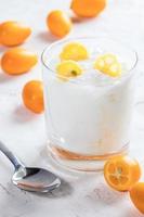 Transparent glass with white fat yogurt with kumquat slices and metal spoon on white  background. photo