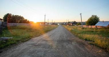 Sun-drenched ground road leading to river in village at sundown in Russia. photo