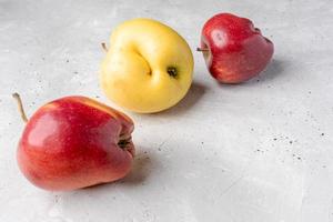 tres feas manzanas rojas y amarillas yacen caóticamente sobre un fondo de hormigón gris. foto