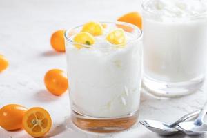 dos vasos con yogur con rodajas de kumquat y dos cucharas sobre fondo blanco. foto