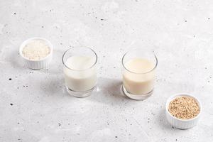 Glasses with rice and oat milk, bowls with rice seeds and oat flakes on concrete background. photo