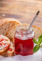 tarro de cristal con mermelada de fresa, pan, tostadas con cuajada y mermelada en servilleta blanca sobre mesa de madera. foto