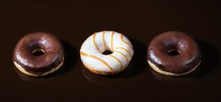 Three glazed donuts on dark  chocolate smooth background. photo