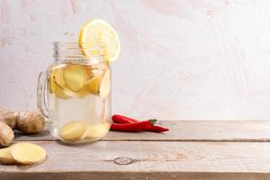 Glass jar with ginger water on wooden table on light background with copy space. photo
