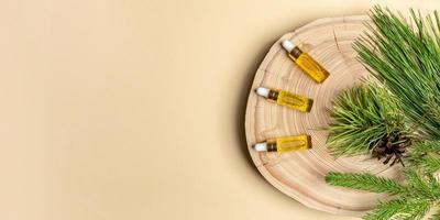 Three small glass bottles with coniferous essential oils of pine, spruce and cedar with branches on wooden cut on beige. photo