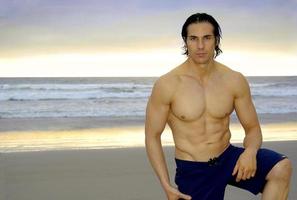 Male muscular surfer poses at Black's Beach, San Diego showing off his defined chest and six-pack abs. photo