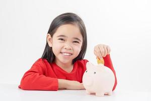 Little Asian girl saving money in a piggy bank, learning about saving, Kid save money for future education. Money, finances, insurance, and people concept photo