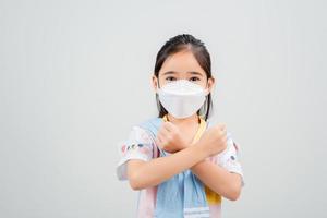 Asian little child girl wearing respirator mask to protect coronavirus outbreak and pointing hand to blank background, New virus Covid-19 photo