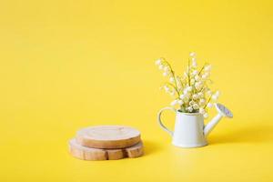 Wooden podium or pedestal with lilies of the valley bouquet in a decorative watering can on a yellow background photo