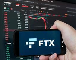 Man holding phone with FTX logo. Global fall of cryptocurrency graph - FTT token fell down on the chart crypto exchanges on app screen. FTX exchange bankruptcy and the collapse depreciation of token. photo