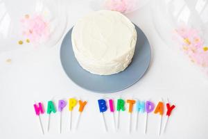 Colorful candles with Happy Birthday lettering isolated on white background along with confetti and bento cake. Holiday and surprise concept. photo