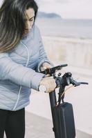 hermosa mujer latina montando su scooter motorizado en la ciudad, activando la aplicación de teléfono inteligente. foto
