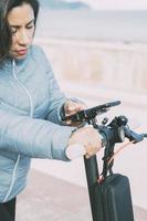 Beautiful latina woman riding her motorized scooter in the city, activating smart phone app. photo