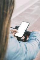 top rear view of latina woman riding electric scooter using smart phone white screen, for apps photo