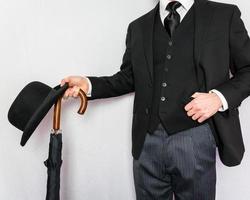 retrato de hombre de negocios en traje oscuro con sombrero y paraguas sobre fondo blanco. caballero inglés clásico y excéntrico. foto