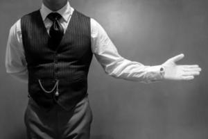 retrato en blanco y negro de un mayordomo bien vestido con guantes blancos con un gesto de bienvenida. concepto de industria de servicios y hospitalidad profesional foto