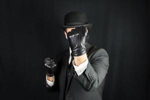 Gentleman in Dark Suit and Leather Gloves with Fists Raised in Fighting Pose on Black Background. Concept of Classic and Eccentric British Gentleman photo