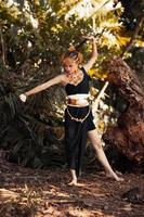 Beautiful Balinese woman holding her black hair while posing in a black dance dress inside the jungle photo