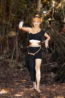 Javanese woman dancing pose in a black tank top and black skirt with golden crown and golden accessories on her body inside the jungle photo