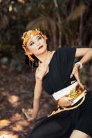 Asian woman poses with her hand while wearing a black dress and a gold belt with a gold crown on her head photo