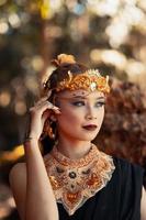 reina tribal maquillada mientras usa una corona de oro y un collar de oro con el vestido negro foto