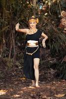 Javanese woman dancing pose in a black tank top and black skirt with golden crown and golden accessories on her body inside the jungle photo