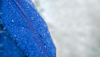 Wide screen of raindrops on blue umbrella with blurry of road on rainy day. photo