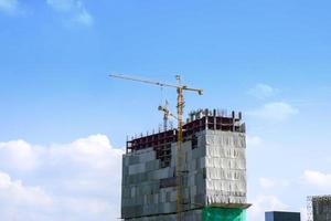 Remote image of a building under construction with hoisting cranes on bright blue sky and cloudy background. photo