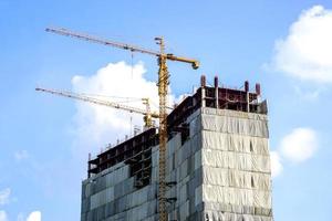 Building under construction with hoisting cranes on bright blue sky and cloudy background. photo