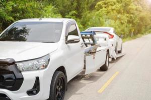 los toboganes de camión de coche dañados de primer plano y el coche blanco en el accidente en la carretera local con bengalas solares y fondo de plantas verdes. foto