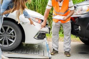 los oficiales de la compañía de seguros de primer plano publican una lista de reparaciones en el portapapeles de la lista de trabajo según la mujer que sufre señala el daño en los antecedentes de su automóvil. foto