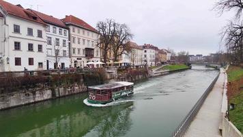 Ljubljana, Slovenia 2022.12.25 Boat passing in the canal on Slovenia capital Ljubljana during a winter cloudy day. Historical and multicultural city. Amazing winter destinations.
