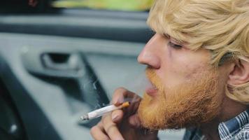 un homme avec une barbe fume dans une voiture. gros plan de fumer dans une voiture debout. inhale et dégage de la fumée de la bouche video