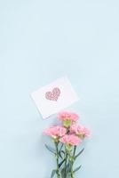 hermosa y elegante flor de clavel rosa sobre fondo de mesa azul claro brillante, concepto de regalo de flores del día de la madre, vista superior, puesta plana, sobrecarga foto