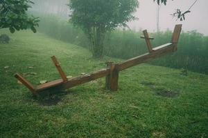 Wooden see saw in the garden with foggy background. Playground in the morning photo