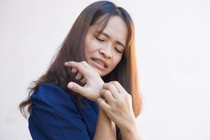 Woman scratching arm from itching on light gray background. Cause of itchy skin include insect bites Concept of health care skin. photo