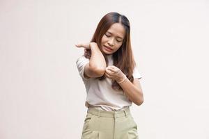 mujer rascándose el brazo por picazón en un fondo gris claro. la causa de la picazón en la piel incluye el concepto de picaduras de insectos de la piel para el cuidado de la salud. foto